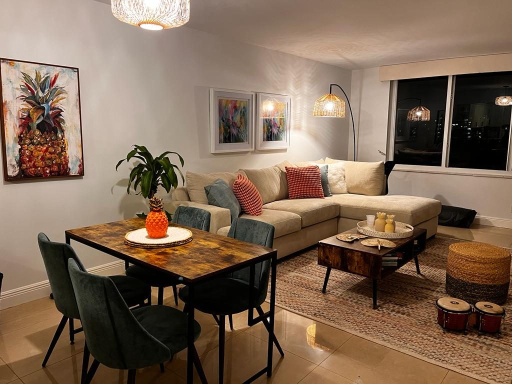 Sala y comedor decorados por Ana Granada: sofá en L color arena con cojines rojos, mesa de madera, tapete de fibra y cuadros en las paredes